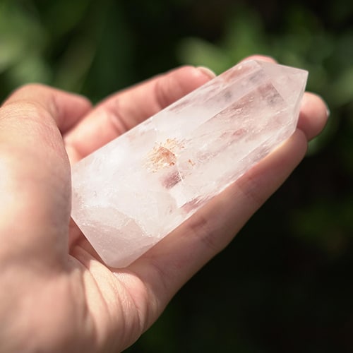 Woman holding large clear crystal outside near trees